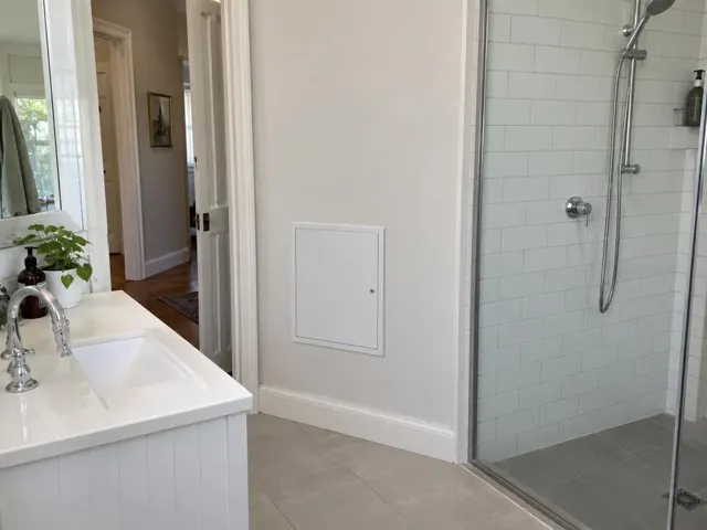 Bathroom wall with a small access panel beside a tiled shower and vanity in Kensington